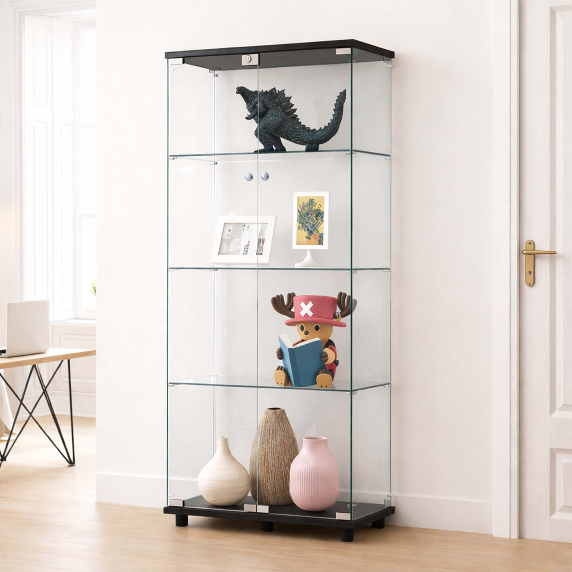 A tall glass display cabinet with black top and bottom frames, shown in a bright room with shelves holding a dinosaur figurine, framed art, a small plush toy, and three vases.